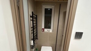 Ein kleines, schmales Badezimmer mit Toilette, Waschbecken und Spiegel.