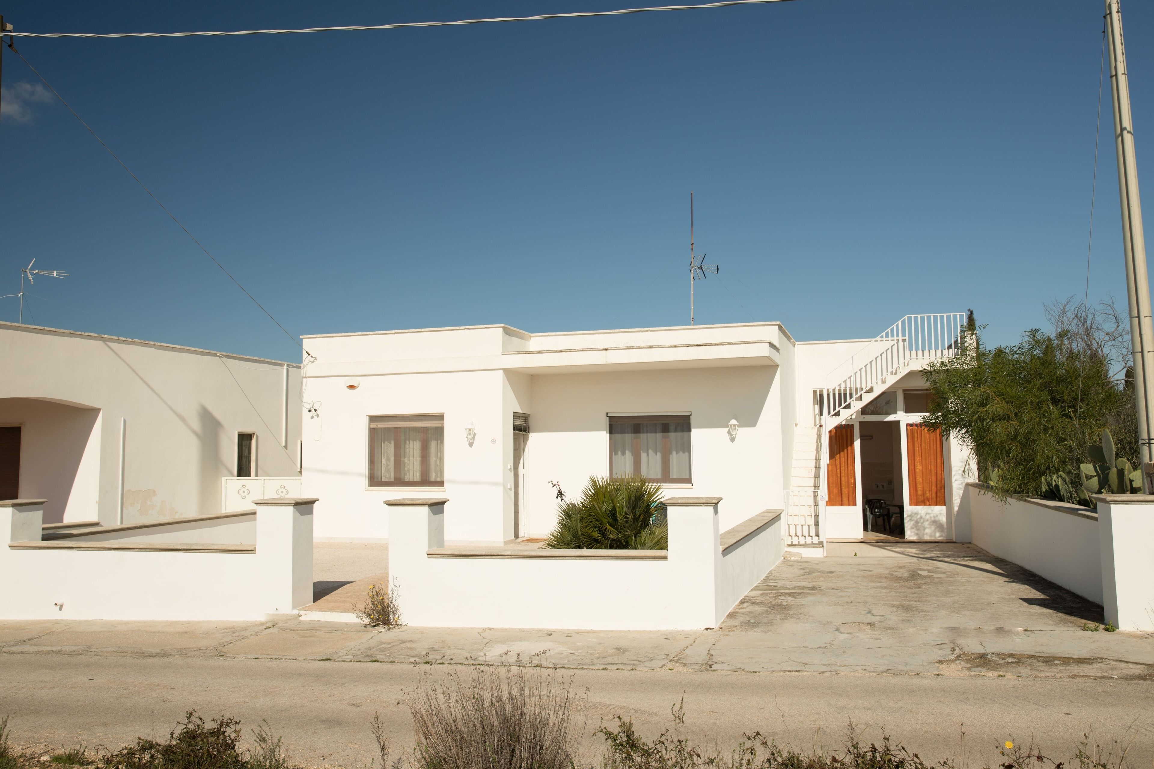 A white two-story house with a balcony, a staircase, and a small garden area.