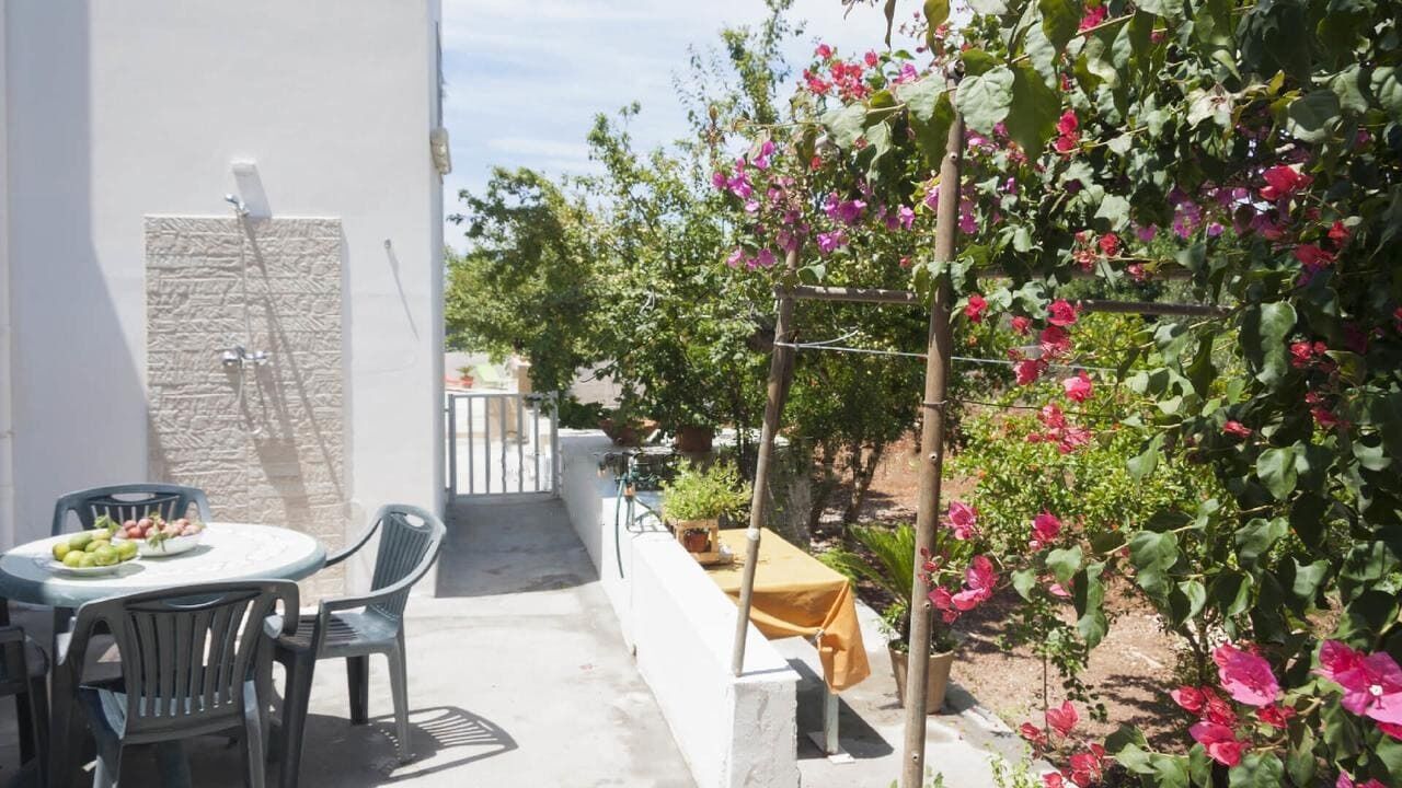 An outdoor patio with a table and chairs, a small garden with flowering plants, and a wall-mounted water feature.