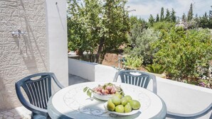 Une table ronde, sur laquelle se trouvent un saladier de fruits et une assiette de pommes vertes, est placée sur une terrasse dotée d’un mur en pierre et agrémentée de plantes en pot.
