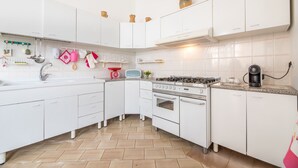 Une cuisine moderne avec des meubles blancs, une cuisinière à gaz, un four et une machine à café.