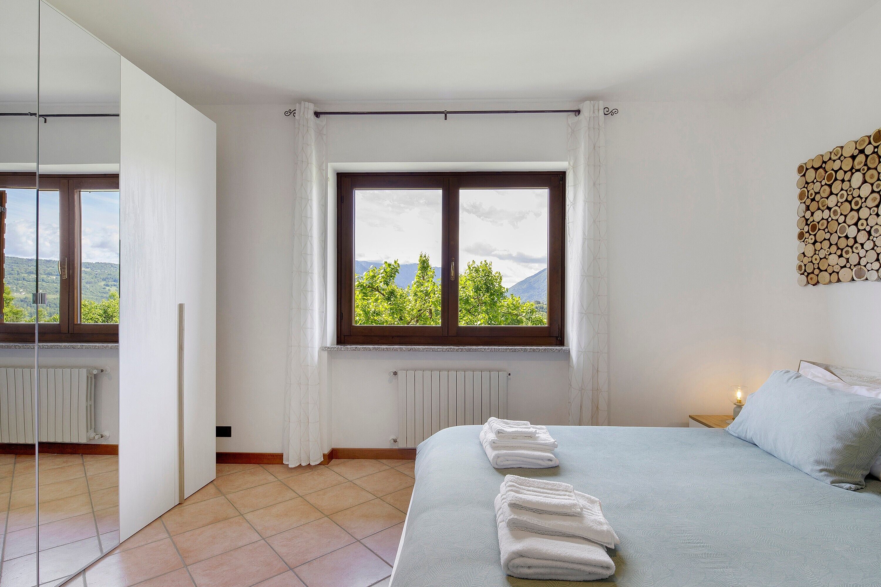 Une chambre à coucher avec un lit, une fenêtre donnant sur un beau paysage, un radiateur et une table de chevet avec une lampe.