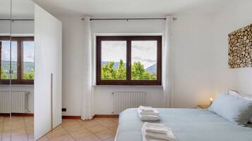 Une chambre à coucher avec un lit, une fenêtre donnant sur un beau paysage, un radiateur et une table de chevet avec une lampe.