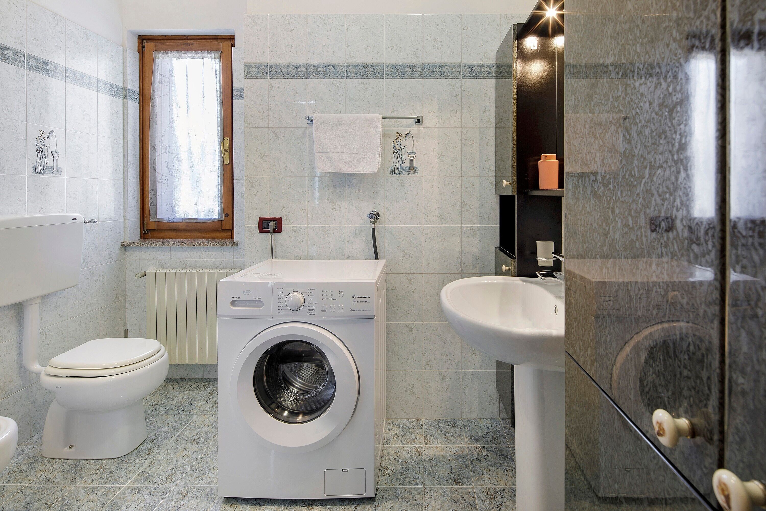 Une salle de bain équipée d’un lave-linge, de toilettes, d’un lavabo et d’une fenêtre.