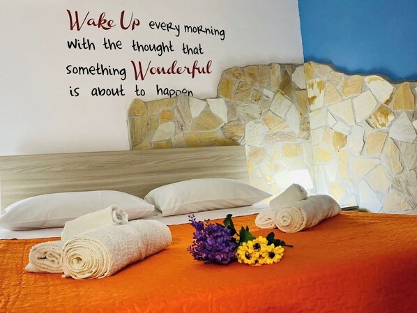 A neatly made bed with rolled white towels, a stone wall, and a motivational quote on the wall.