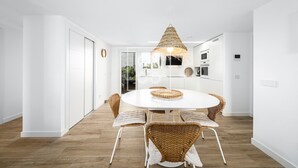 Une cuisine moderne avec des meubles blancs, une table de salle à manger ronde, des chaises en osier et un luminaire suspendu.