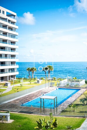 A modern hotel with a pool area, palm trees, and a view of the ocean. - Beachfront Bliss apt, with heated pool, by OYOOSTAYS (Torrevieja)