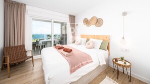 Une chambre avec un lit, une chaise, une petite table avec des plantes et une vue sur la mer, visible à travers une porte coulissante.