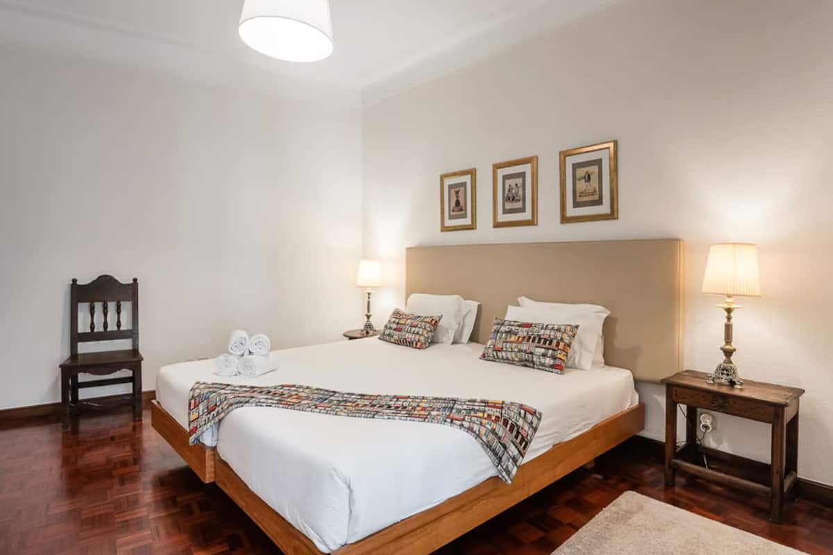 Een opgemaakt bed met een geborreld deken, twee bedlampjes en een houten nachtkastje.