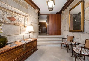 A hallway with a wooden desk, a lamp, and two chairs.
