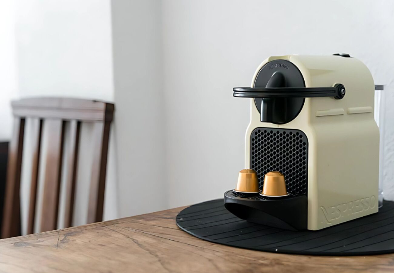 A Nespresso coffee machine on a wooden table with a black mat.