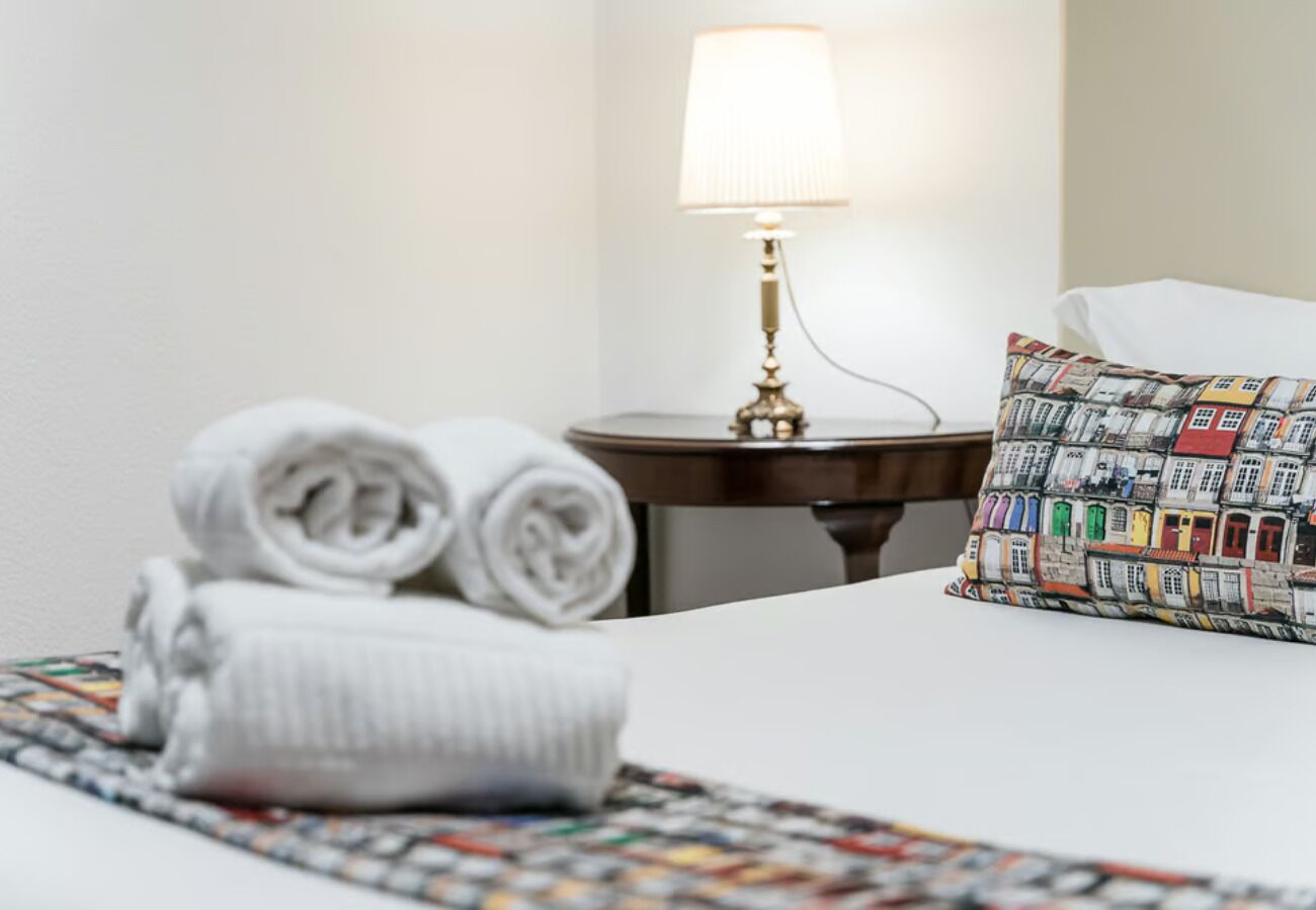 A neatly made bed with rolled towels, a colorful pillow, and a bedside lamp on a small table.
