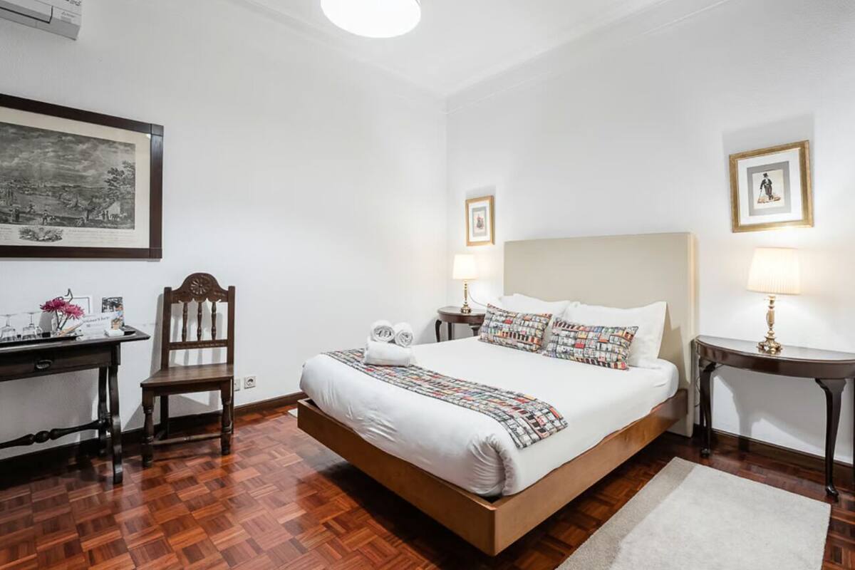 Een verzorgde hotelkamer met een groot bed, een bureau en een stoel. Er zijn twee nachtkastjes met lampen.