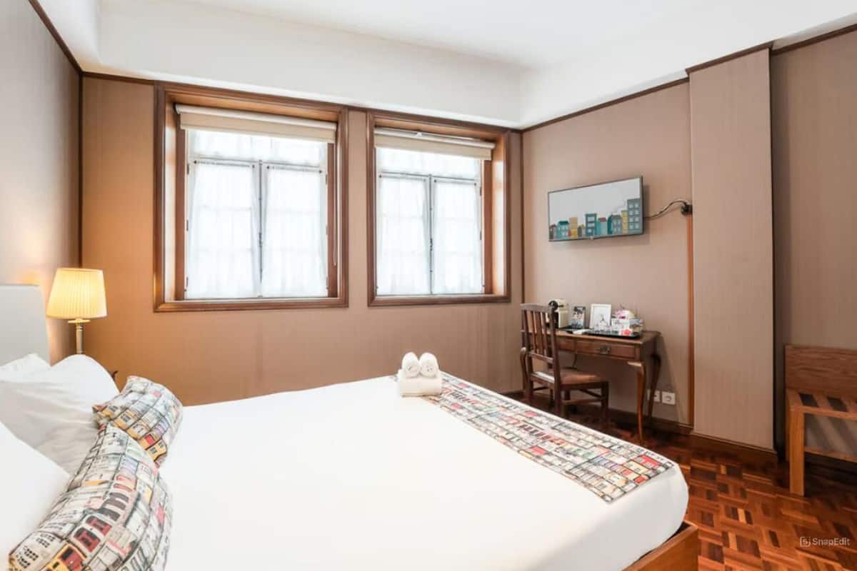 Een hotelkamer met een groot bed, twee ramen, een bureau en een stoel.