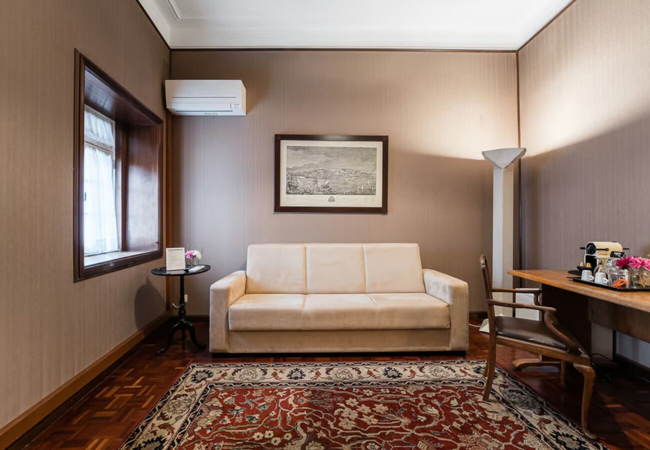 A room with a sofa, a small table with a vase, a framed picture on the wall, and a lamp.