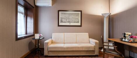 A room with a sofa, a small table with a vase, a framed picture on the wall, and a lamp.
