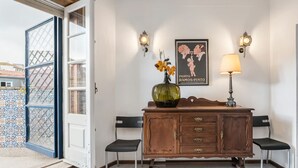 A room with a wooden cabinet, two chairs, a vase with flowers, and a poster on the wall.