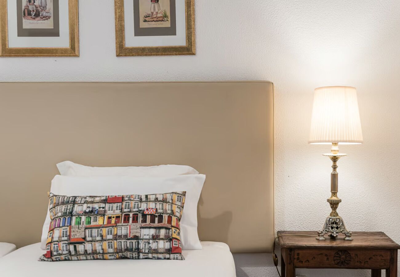 A neatly made bed with a patterned pillow, a bedside table with a lamp, and two framed pictures on the wall.