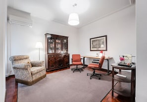 A room with a patterned armchair, a wooden cabinet, a desk with a chair, and a lamp. - Office Residence (Porto)