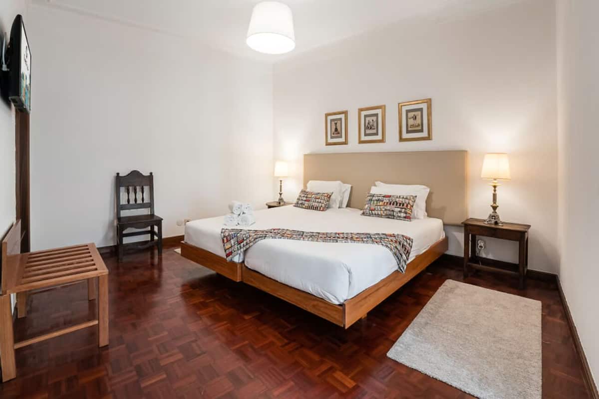 Een slaapkamer met een houten bed, een houten bankje, een stoel en een nachtkastje met een lamp.