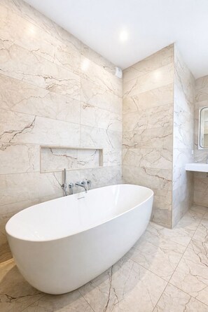 Un baño moderno con una bañera independiente, paredes de mármol y un lavamanos empotrado.