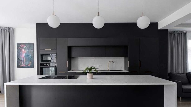 Een moderne keuken met een groot eiland, donkere kastjes en hanglampen.