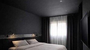 Een moderne slaapkamer met een groot bed, donkere wanden en een plafondlamp.
