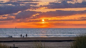 Een strand met een zonsondergang, een zeilboot en mensen die wandelen.
