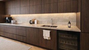 A modern kitchen with dark wood cabinets, a granite countertop, a built-in oven, and a wine bottle on the counter. - Sophisticated 3-Bed Residence for 6 | Urban Calm (London)