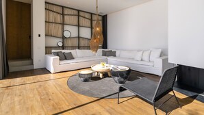 Ein modernes Wohnzimmer mit einem weißen Sofa, einem runden Couchtisch und einem schwarzen Sessel. Eine gewebte Leuchte hängt über dem Tisch.