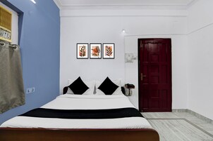 A bedroom with a bed, a red door, and three framed pictures on the wall.