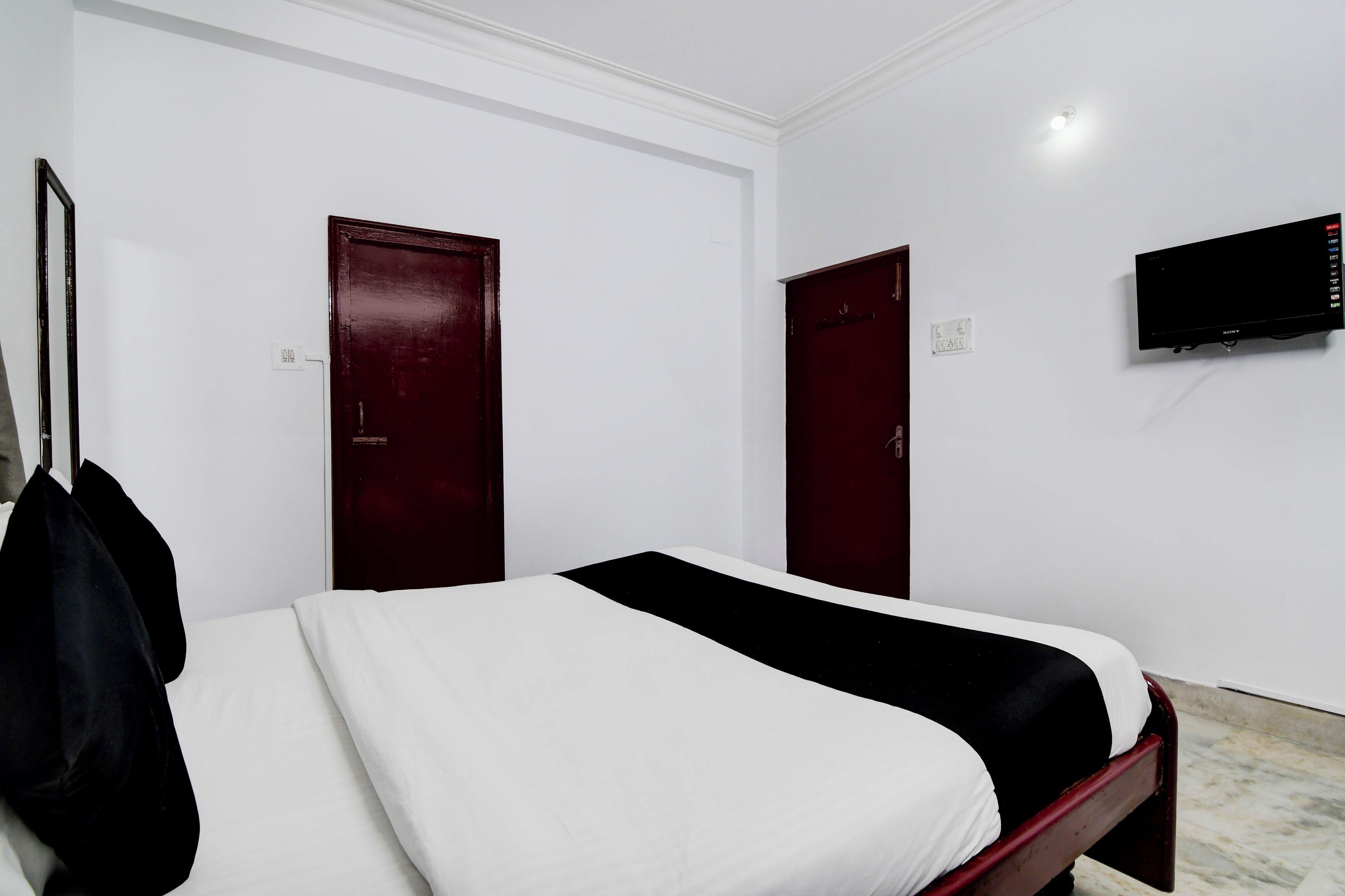 Una habitación de hotel con una cama, dos puertas, un televisor y un perchero.
