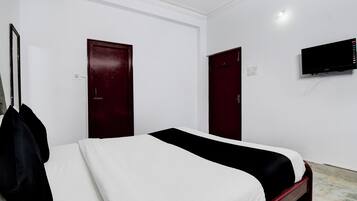 Una habitación de hotel con una cama, dos puertas, un televisor y un perchero.