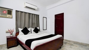 A neatly arranged bedroom with a bed, a nightstand, an air conditioning unit, a mirror, and a door. - Smart stay by- Brill rooms (Barasat)