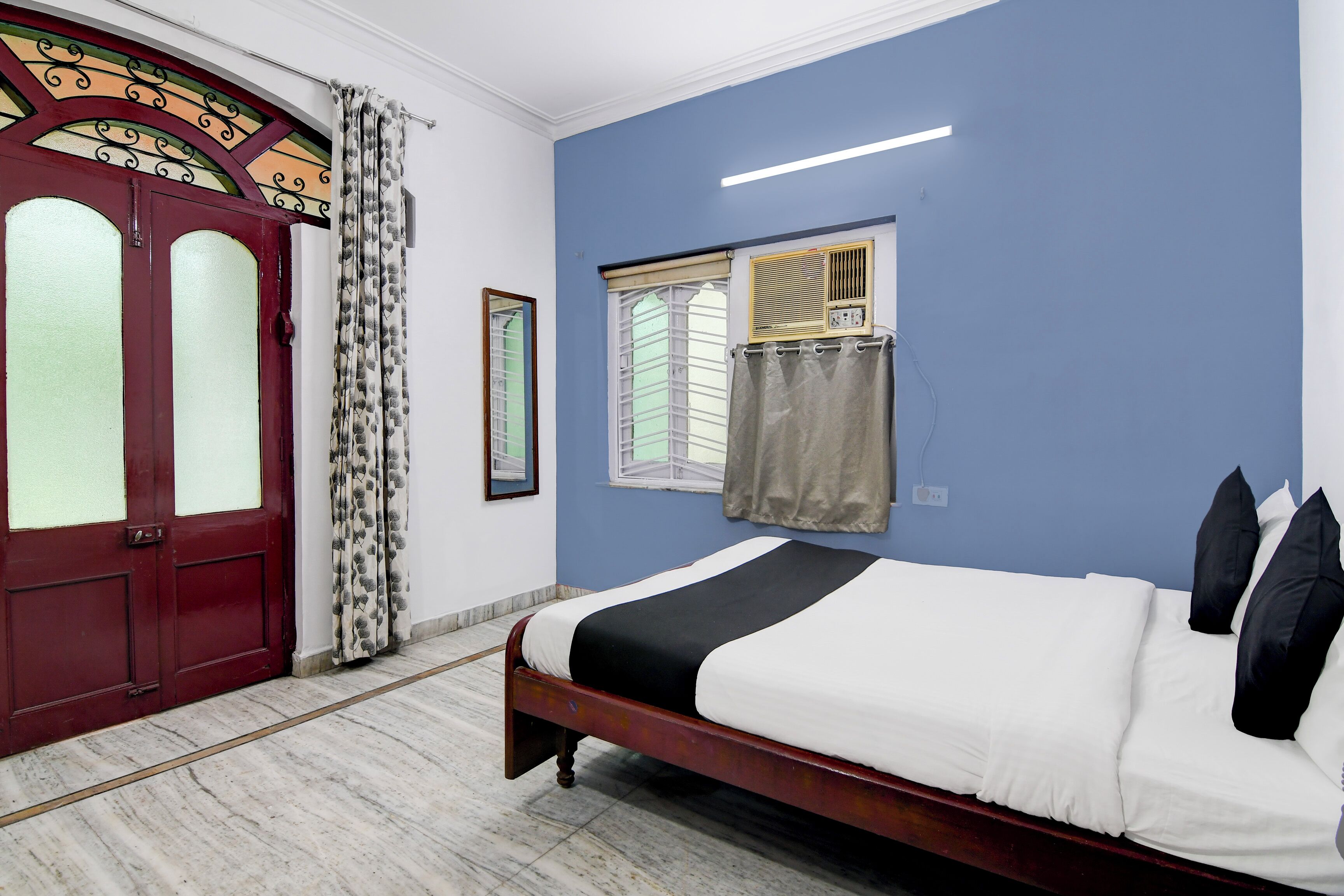 A bedroom with a bed, a window with curtains, a radiator, and a door with decorative glass panels.