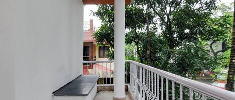 A balcony with a white railing, a bench, and a view of a building with a red roof.