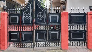 A black metal gate with decorative elements and a red wall. - Smart stay by- Brill rooms (Barasat)