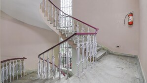 A staircase with ornate white railings and a red handrail, leading to a landing with a fire extinguisher mounted on the wall. - Smart stay by- Brill rooms (Barasat)