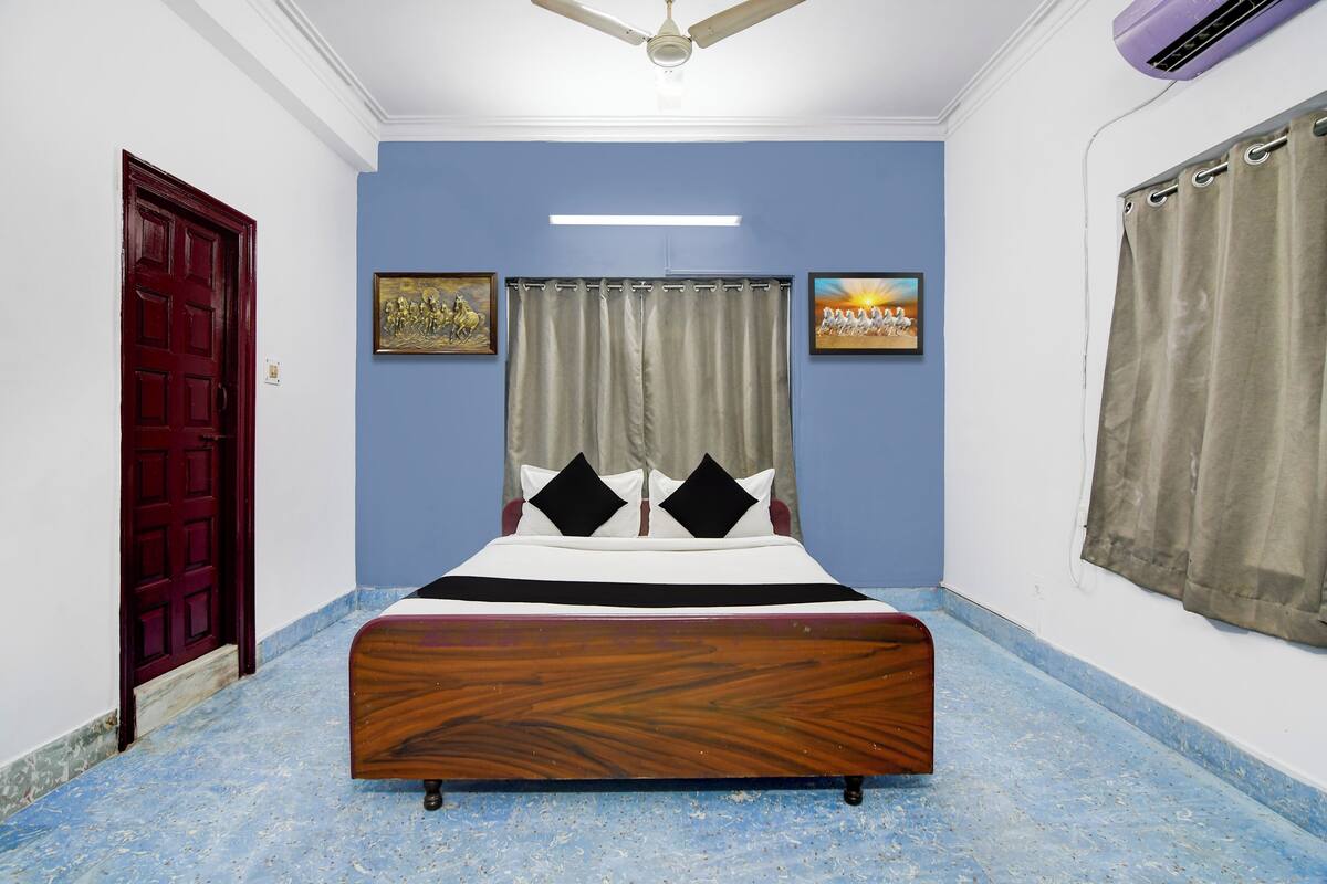 A bedroom with a wooden bed, blue walls, a red door, and two framed pictures.