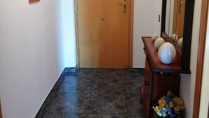 Käytävä, jossa on puinen ovi, seinälle asennettu puhelin, kehystetyt valokuvat ja koriste-esineillä koristeltu konsolipöytä.