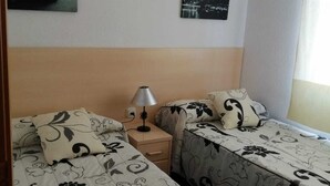 Hotellihuoneessa on kaksi sänkyä, joissa on kummassakin kukkakuviollinen vuodevaatesetti. Sänkyjen välissä on yöpöytä, jossa on lamppu, ja seinällä on kuva autosta ja kaupunkimaisemasta.