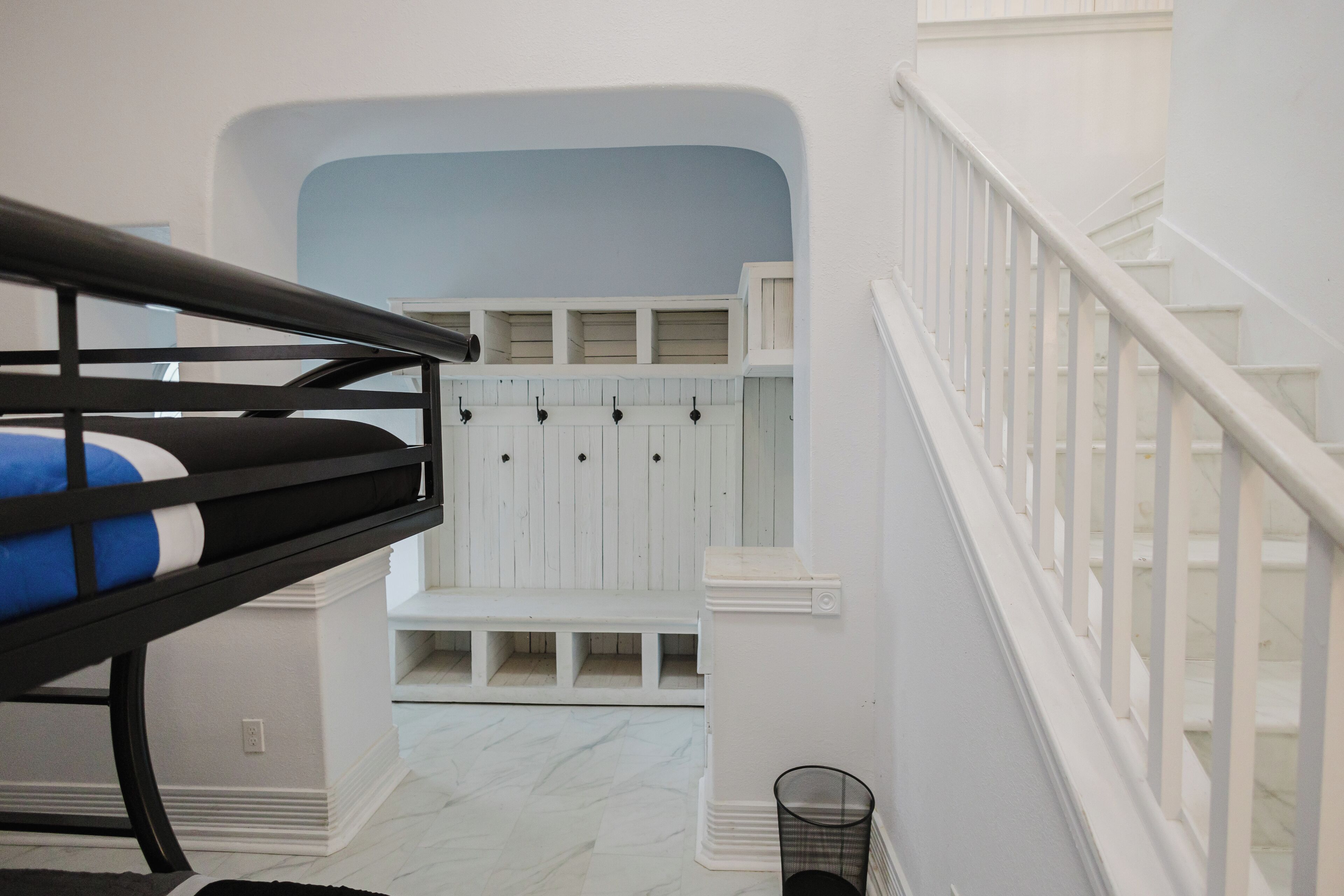 Un lit superposé avec un matelas bleu, un escalier blanc avec une rampe et un mur blanc agrémenté d’une touche de bleu.