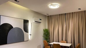 A modern dining area with a table and chairs, an air conditioning unit, a large abstract painting, and a plant. - GREYFIELD APARTMENT 2 (Benin City)