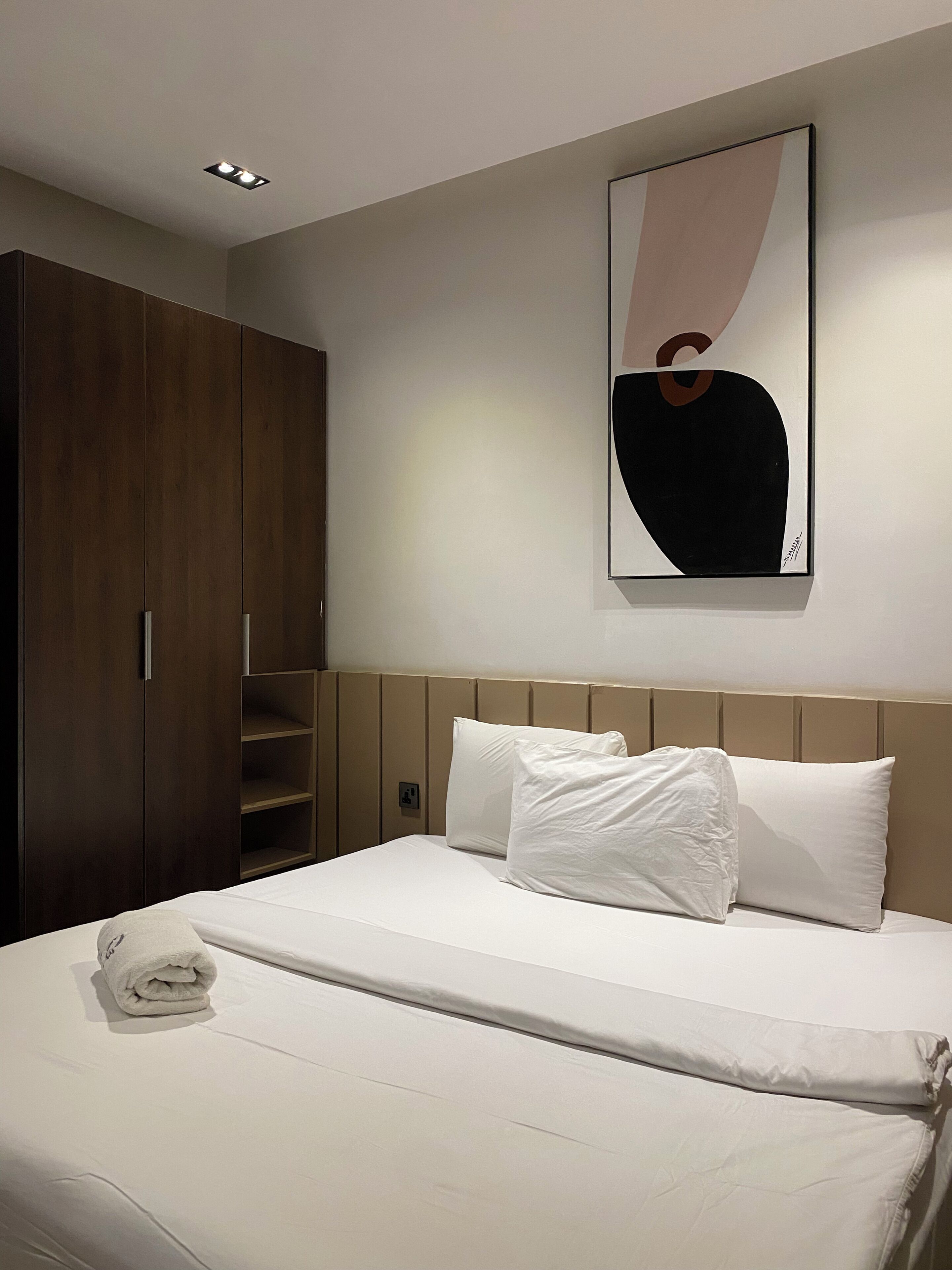 A hotel room with a bed, a wardrobe, and a wall-mounted abstract artwork.