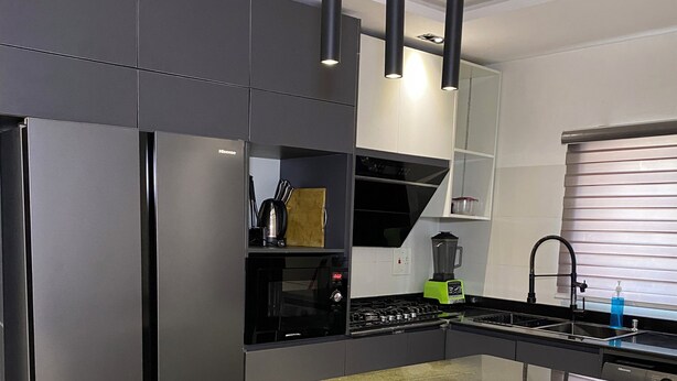 A modern kitchen with a central island, stainless steel appliances, pendant lighting, and a built-in stove. - GREYFIELD APARTMENT 2 (Benin City)