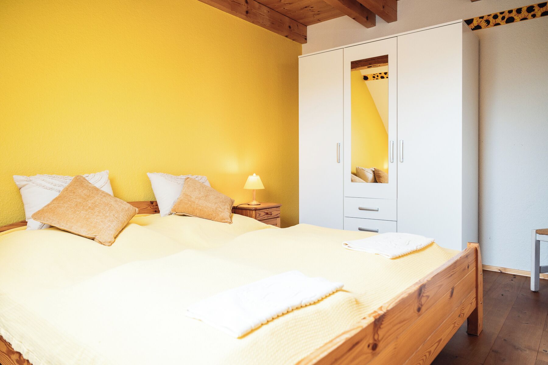 Een slaapkamer met een bed, kussens, een nachtkastje, een lamp en een kledingkast.