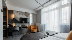 Habitación de hotel con cama, escritorio, silla, televisor y ventana con cortinas.