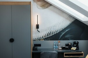 Una habitación moderna con escritorio, teléfono, botellas de agua, cafetera y un cuadro en la pared.