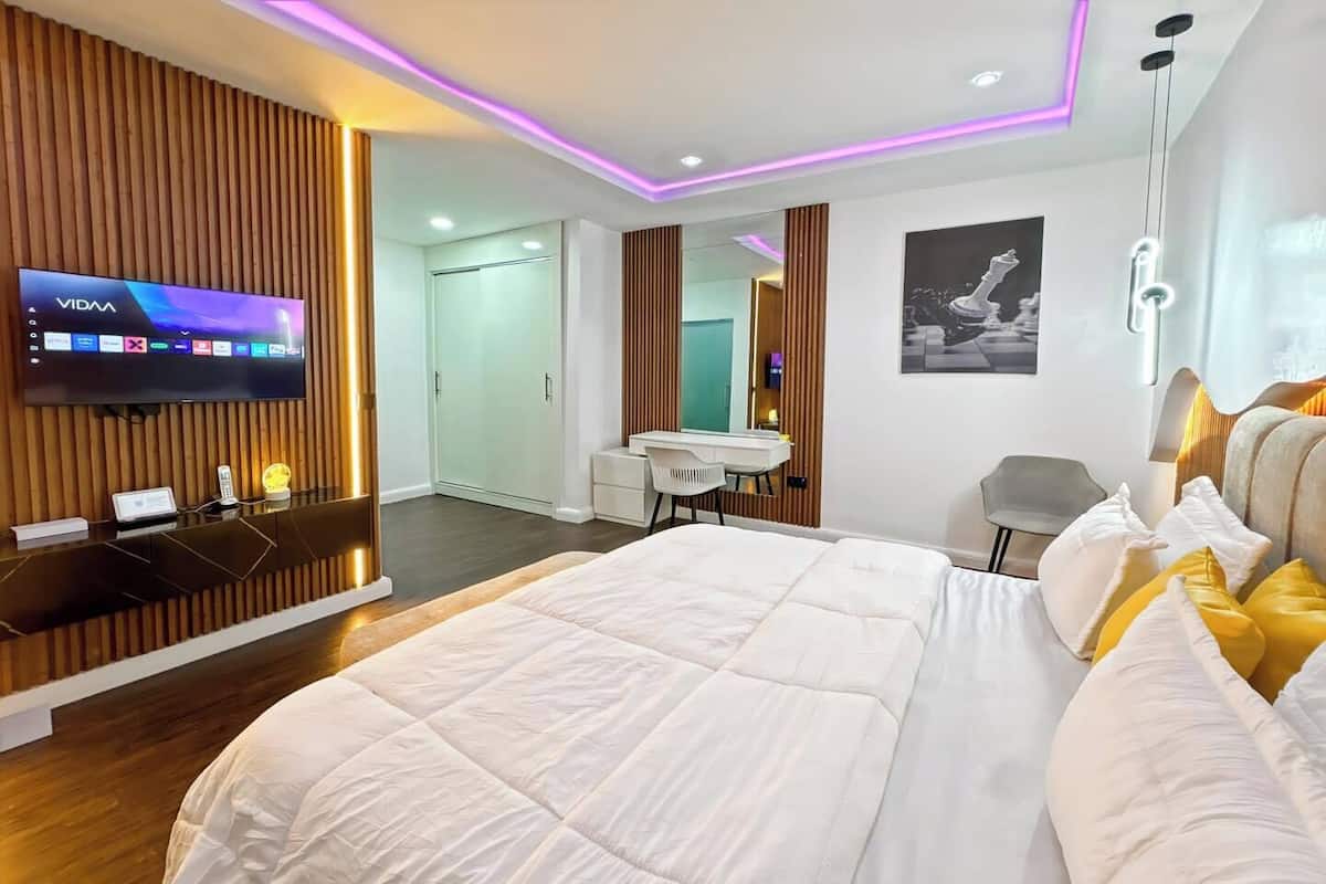 A modern hotel room with a large bed, a desk, a TV, and a mirror.
