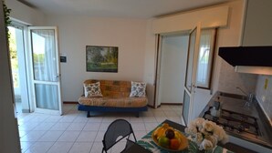 Un espacio habitable pequeño con sofá, una mesa de comedor con fruta, una zona de cocina y un cuadro en la pared.